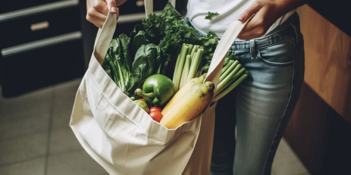 Woman holding reusable grocery bag filled with fresh vegetables