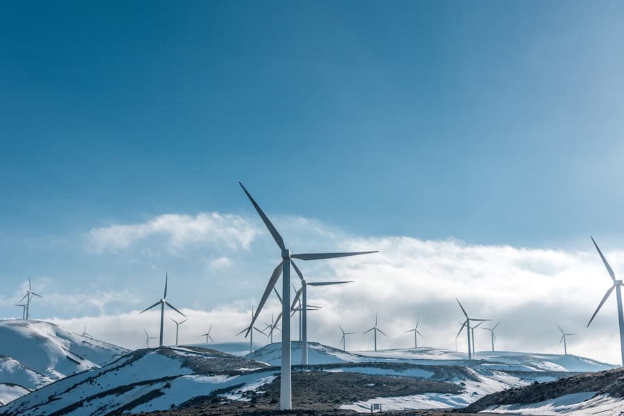 Tall wind turbines on snowy mountain landscape under blue sky, renewable energy, sustainable eco-friendly technology, green energy source, eco conscious living.
