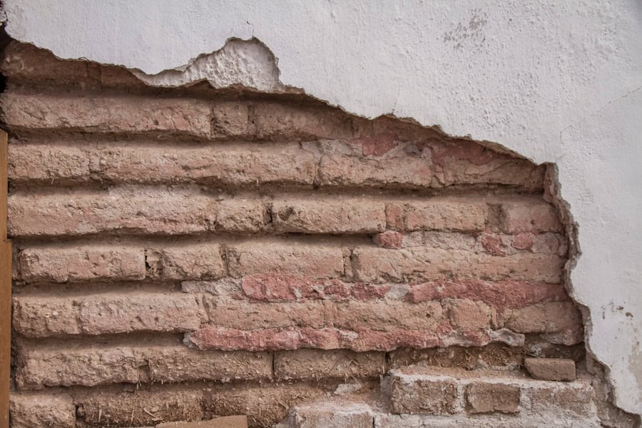 Cracked brick wall showing insulation layers behind plaster, eco-friendly home repair, sustainable building materials, energy-efficient wall restoration, eco-conscious renovation techniques.