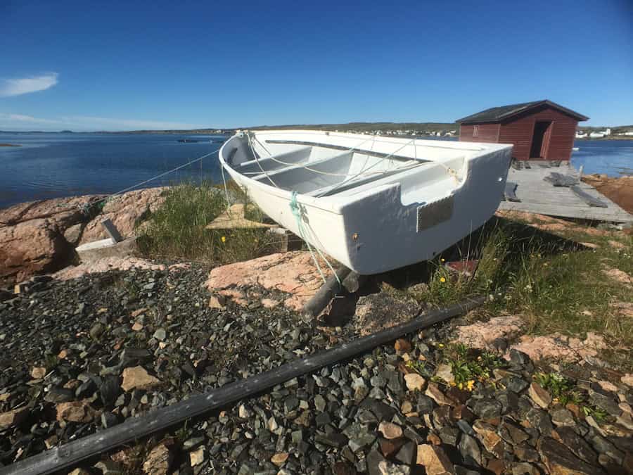 Small white boat on rocky shoreline with calm water and sky in background, eco-friendly sustainable fishing or boating scene.