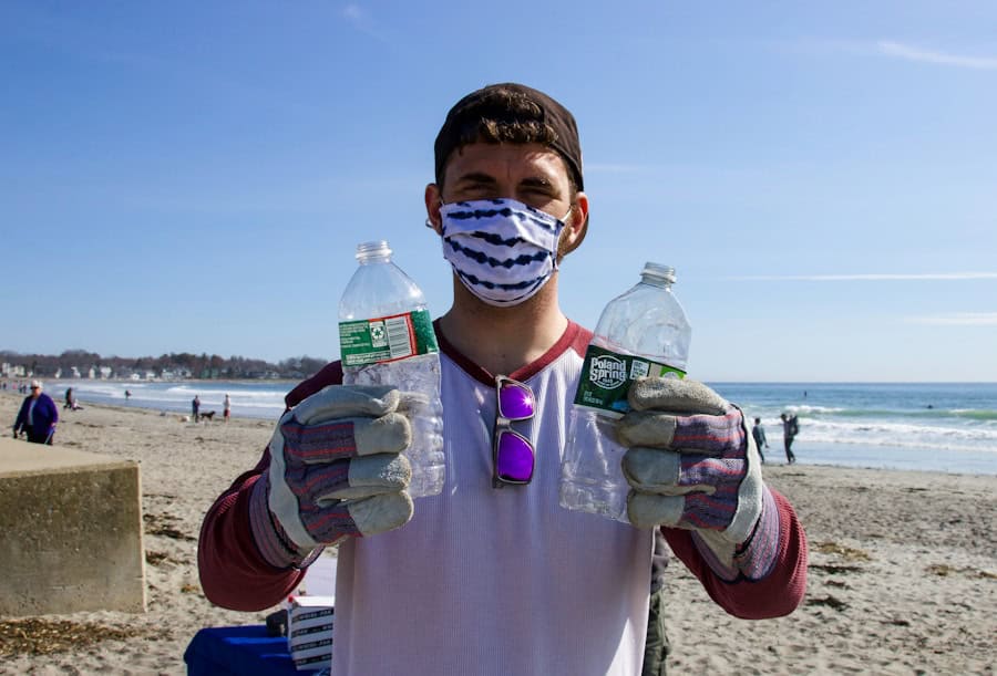 Reusable plastic bottles on a clean beach with a person wearing eco-friendly mask and gloves, promoting sustainability and reduction of plastic waste.