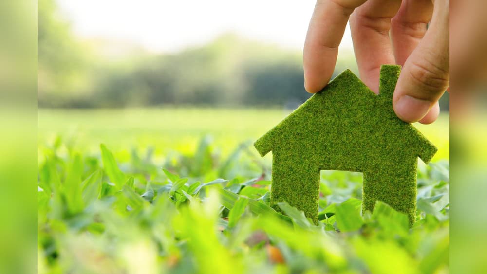 Eco-friendly house cutout held above green grass, symbolizing sustainable living and eco-conscious home solutions.